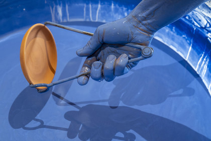 France, Nièvre, Nevers, Fayencerie d’art de Nevers, master earthenware maker Clair Bernard dips the biscuit using a metal claw into the Bleu de Nevers enamel bath