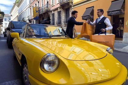 Italy, Lombardy, Milan, Fashion Quadrilateral (Quadrilatero della moda), Alfa Romeo Duetto Spider yellow cabriolet in front of the Four Seasons Hotel Milano, the doorman brings a Vuitton bag