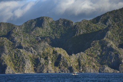 Philippines, Calamian Islands in northern Palawan, Coron Island Natural Biotic Area, outrigger canoe under giant walls of Permian Limestone of Jurassic origin cliffs
