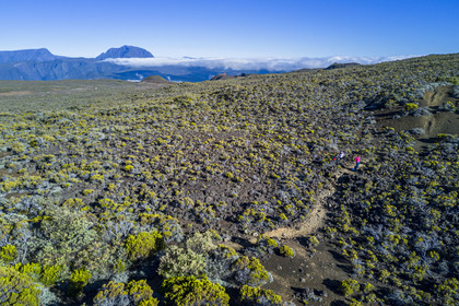 France, Ile de la Reunion, Parc National de la Réunion classé Patrimoine Mondial de l'UNESCO, sur les pentes du volcan de Piton de la Fournaise, randonneur sur le sentier de l'oratoire Ste Thérèse au dessus de la Plaine des Sables, le Piton des Neiges en arrière plan au nord (vue aérienne)
