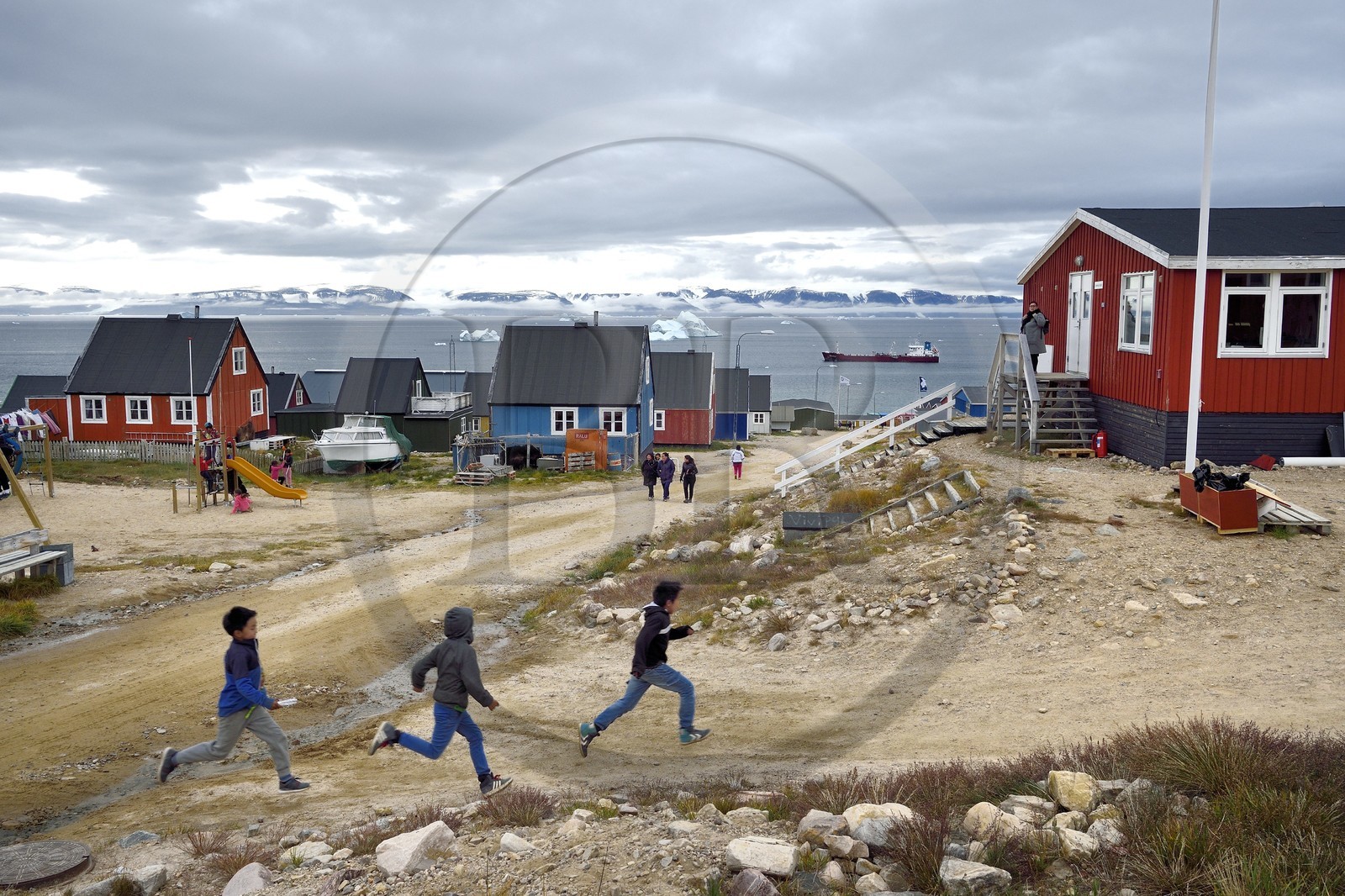 Groenland, cote Nord-Ouest, mer de Baffin, Qaanaaq ou Nouvelle Thule, des enfants inuit courent rejoindre leur maitresse d'école, un iceberg en arrière plan
