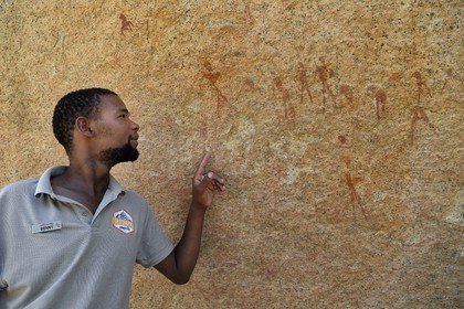 Namibia, Erongo region, Damaraland, the Pondok Mountains at the east of Spitzkoppe in the Namib Desert, rock paintings under a granitic overhang called the Bushman's Paradise believed to have been made between 4,400 BCE and 100 AD, Benny the local Damara guide shows human figures