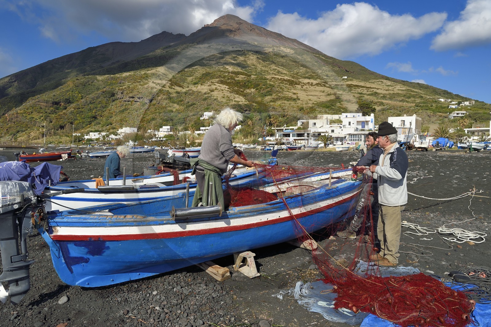 Italie, Sicile, iles Eoliennes, classées Patrimoine Mondial de l'UNESCO, ile de Stromboli, le pecheur Gaetano Cusolito réparant ses filets avec ses deux frères sur la plage de Scari et le volcan du Stromboli en arrière plan