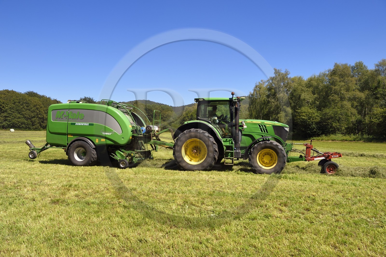 France, Puy-de-Dôme (63), Saint-Ours-les-Roches, hameau de Beauregard, tracteur récoltant le fourrage avec une presse enrubanneuse de balles de foin dans un champ