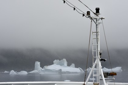 Greenland, west coast, Disko Island, iceberg in the mist off Qeqertarsuaq and bow of the boat