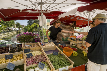 France, Vaucluse, L'Isle sur la Sorgue, market day, Justin serves a customer from his fruit and vegetable stall on a bridge over the Sorgue river