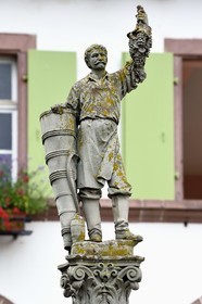 France, Haut Rhin, the Alsace Wine Route, Ribeauville, statue on a fountain of a wine grower leaning on his basket and presenting in his left hand a beautiful bunch of grapes