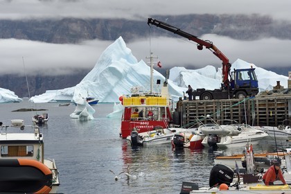 Groenland, cote ouest, Uummannaq, bateau de pêche déchargeant dans le port et icebergs en arrière plan