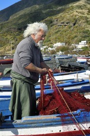 Italie, Sicile, iles Eoliennes, classées Patrimoine Mondial de l'UNESCO, ile de Stromboli, le pecheur Gaetano Cusolito réparant ses filets sur la plage de Scari et le volcan du Stromboli en arrière plan