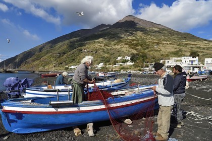 Italie, Sicile, iles Eoliennes, classées Patrimoine Mondial de l'UNESCO, ile de Stromboli, le pecheur Gaetano Cusolito réparant ses filets avec ses deux frères sur la plage de Scari et le volcan du Stromboli en arrière plan