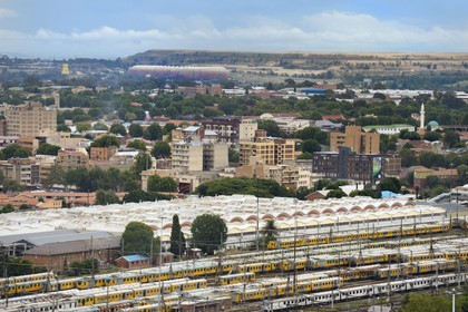 South Africa, Gauteng Province, Johannesburg, colorfull train carriages at Park Station and the Soccer City Stadium in Soweto at the foot of a huge gold mine's spoil tip in the background