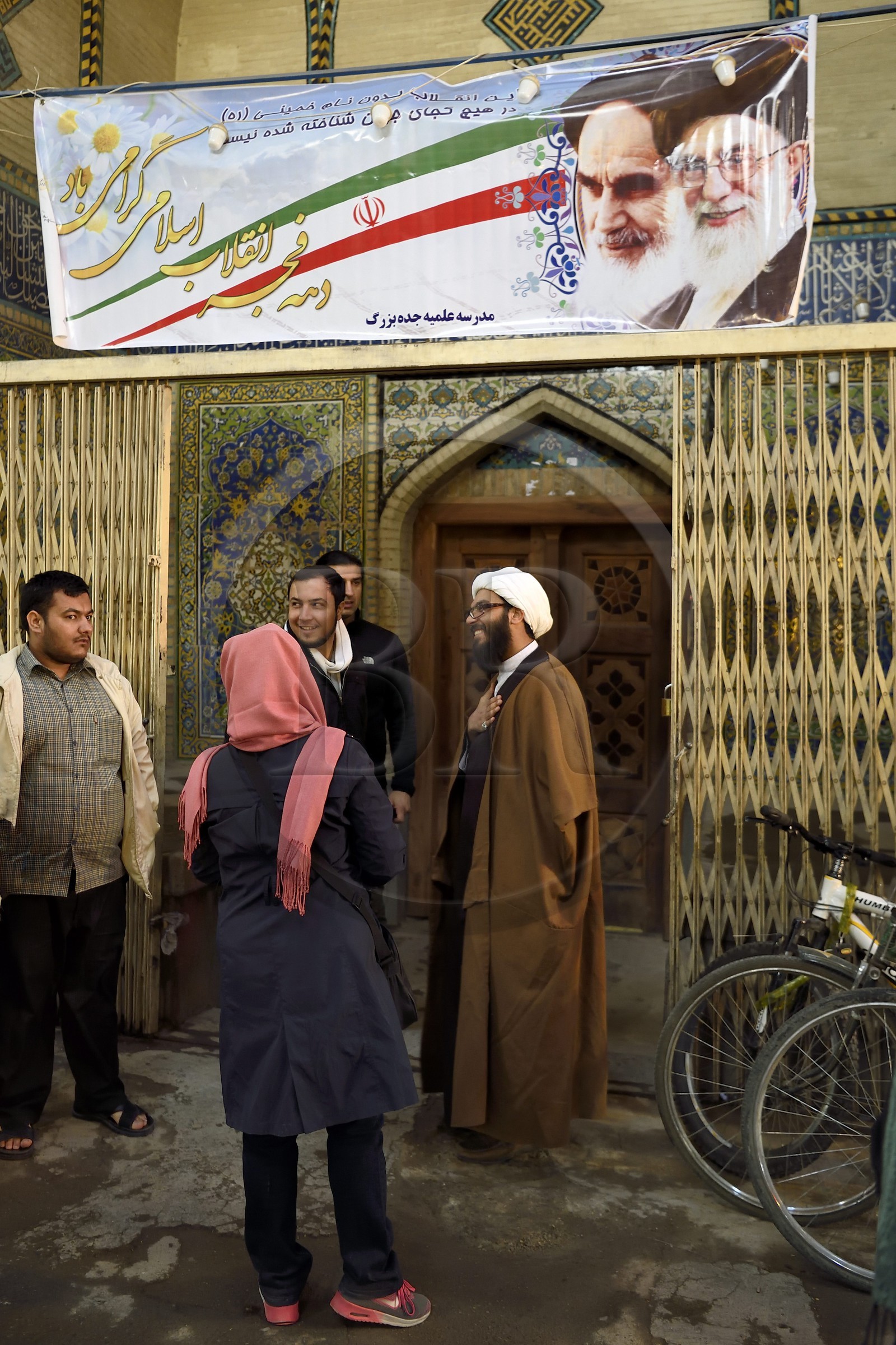Iran, province d'Ispahan, Ispahan, mollah dans le Bazar-e Bozorg (Grand Bazar), immense bazar couvert qui remonte à près de 1300 ans, mollah à l'entrée d'une madrassa et sous une affiche mettant à l'honneur les deux guides de la Révolution l'ayatollah Khomeini et l'ayatollah Khamenei (à droite)