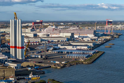 France, Loire Atlantique, Saint Nazaire, the wind turbine towers and blades are stored before embarkation, the 333m MSC World America cruise ship built by Chantiers de l'Atlantique in the background (aerial view)