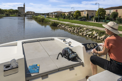 France, Gard, Aigues-Mortes, navigation of a pleasure boat Le Boat on the Canal du Rhône à Sète, the Constance Tower and the ramparts in the background