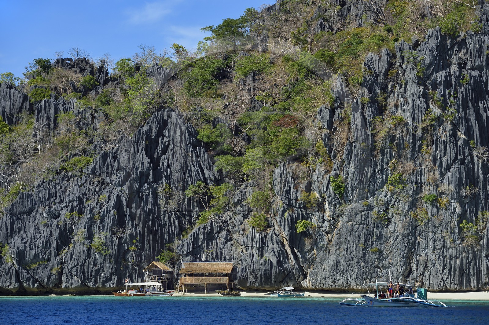 Philippines, Calamian Islands in northern Palawan, Coron Island Natural Biotic Area, Outrigger canoe and beach under giant walls of limestone cliffs