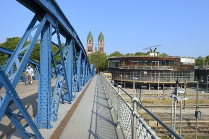 Germany, Baden-Wurttemberg, Freiburg im Breisgau, cyclist on the blue bridge (wiwili-bridge), the Sacred Heart of Jesus Church (Herz-Jesu-kirche) and the Bicycle station called Mobile at the Central Station in the background