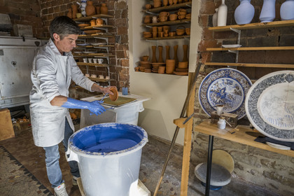 France, Nièvre, Nevers, Fayencerie d’art de Nevers, master earthenware maker Clair Bernard dips the biscuit using a metal claw into the Bleu de Nevers enamel bath
