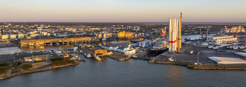 France, Loire Atlantique, Saint Nazaire, the former German submarine base built during the last world war border the dock of the harbour basin of Saint-Nazaire, the East lock and the fortified lock in the foreground and the construction site of the luxury super-yacht Ritz-Carlton Luminara in the Joubert dry dock on the right, the wind turbine towers are stored before embarkation (aerial view)
