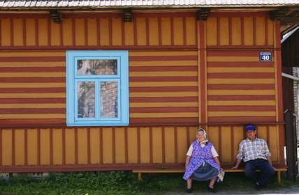 Poland, Lesser Poland, Carpathian Mountains, country woman sitting in front of her wooden painted house in the village of Debno