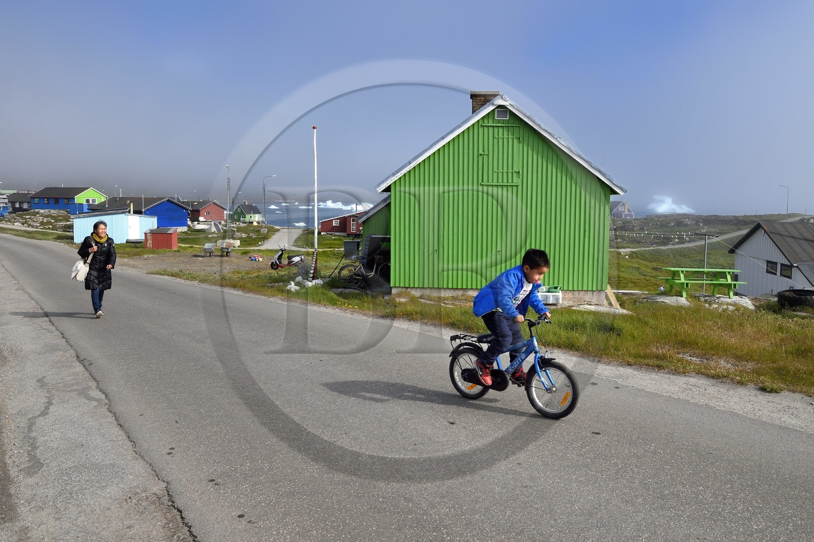 Groenland, cote ouest, Ile de Disko, maisons du village de Qeqertarsuaq et icebergs en arrière plan, enfant à bicyclette