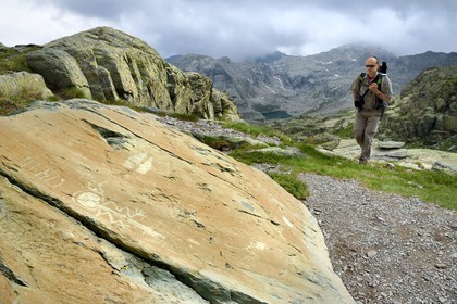 France, Alpes-Maritimes, parc national du Mercantour (Mercantour National Park), the Vallee des Merveilles (Valley of Wonders) scattered with thousands of rupestral engravings of the Bronze Age, Pas de l'Arpette (Arpette pass), hiker approaching the engraving called the zigzag arm Anthropomorphous, a checkerboard-like figure that could symbolize cultivated fields left and two daggers