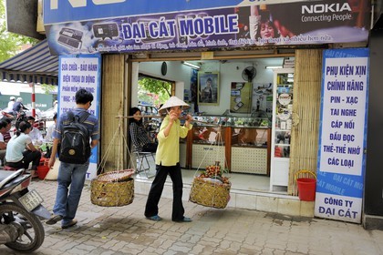 Vietnam, Hanoï, vieille ville, marchande de fruits (lychee) avec sa palanche devant une boutique de téléphones mobiles