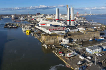 France, Loire Atlantique, Saint Nazaire, the East lock and the fortified lock of the former German submarine base built during the last world war in the foreground and the construction site of the luxury super-yacht Ritz-Carlton Luminara in the Joubert dry dock, the wind turbine towers in the background are stored before embarkation (aerial view)