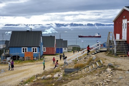 Groenland, cote Nord-Ouest, mer de Baffin, Qaanaaq ou Nouvelle Thule, des enfants inuit courent rejoindre leur école, un iceberg en arrière plan