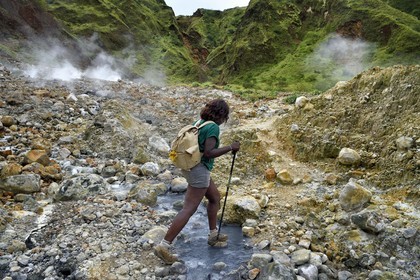 Caraïbes, Ile de la Dominique, Castle Bruce, Parc national du Morne Trois Pitons classé Patrimoine Mondial de l'UNESCO, la Vallée de la Désolation, randonneuse traversant une rivière aux sources d'eau chaude dont la couleur unique est due à la présence de calcium, de carbone, de soufre et de fer, sur le sentier menant au Boiling Lake