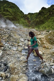 Caraïbes, Ile de la Dominique, Castle Bruce, Parc national du Morne Trois Pitons classé Patrimoine Mondial de l'UNESCO, la Vallée de la Désolation, randonneuse traversant une rivière aux sources d'eau chaude dont la couleur unique est due à la présence de calcium, de carbone, de soufre et de fer, sur le sentier menant au Boiling Lake