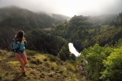 France, Haute Loire, Loire river Valley, Arlempdes, labelized the Most Beautiful Villages of France, hiker observing the ruins of the castle perched on a basalt rock overlooking a Loire river meander