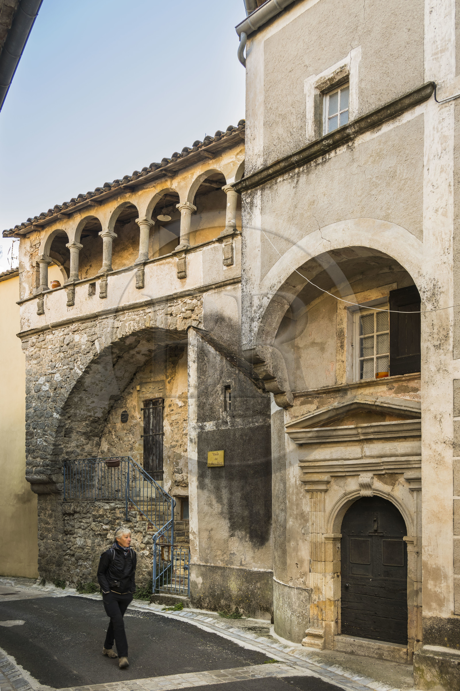 France, Hérault (34), les Causses et les Cévennes, paysage culturel de l'agro-pastoralisme méditerranéen inscrit au Patrimoine Mondial de l'UNESCO, La Vacquerie-et-Saint-Martin-de-Castries, randonneuse passant devant la maison dite du Bailly avec une porte sculptée et une galerie du XVIIème siècle