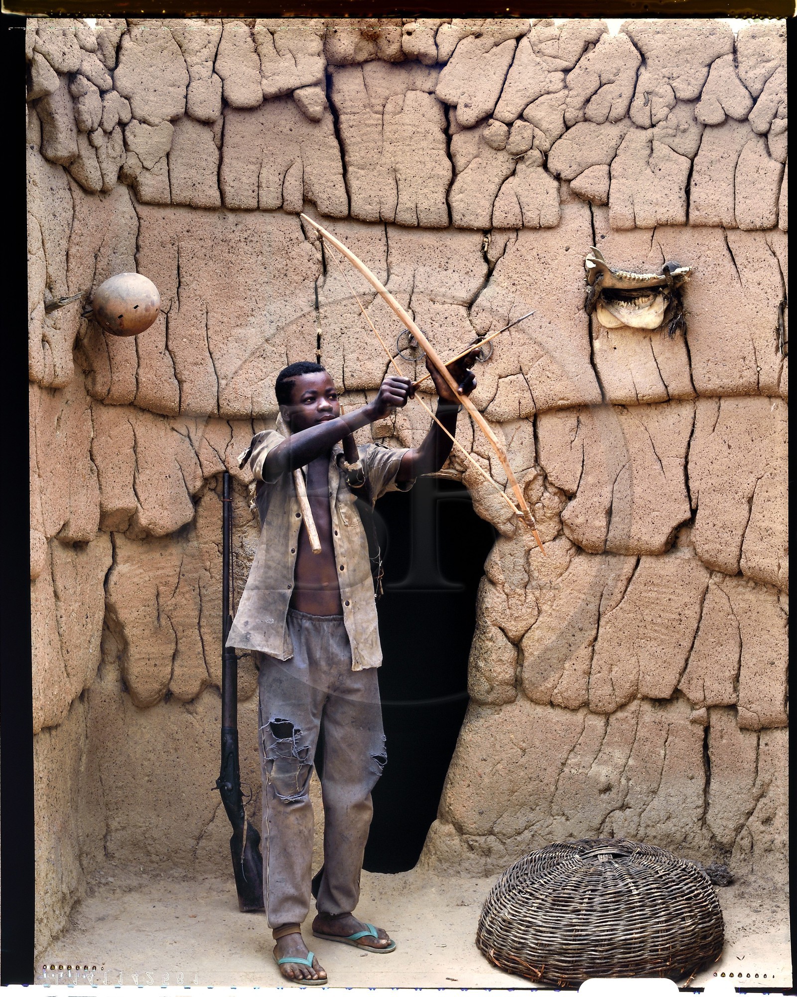 Burkina Faso, province de Poni, pays des Lobi, Loropéni, jeune Lobi devant la maison de son père avec les attributs des initiés: l'arc, le carquois et la houe Burkina Faso, province de Poni, pays des Lobi, Loropéni, jeune Lobi devant la maison de son père avec les attributs des initiés: l'arc, le carquois et la houe
