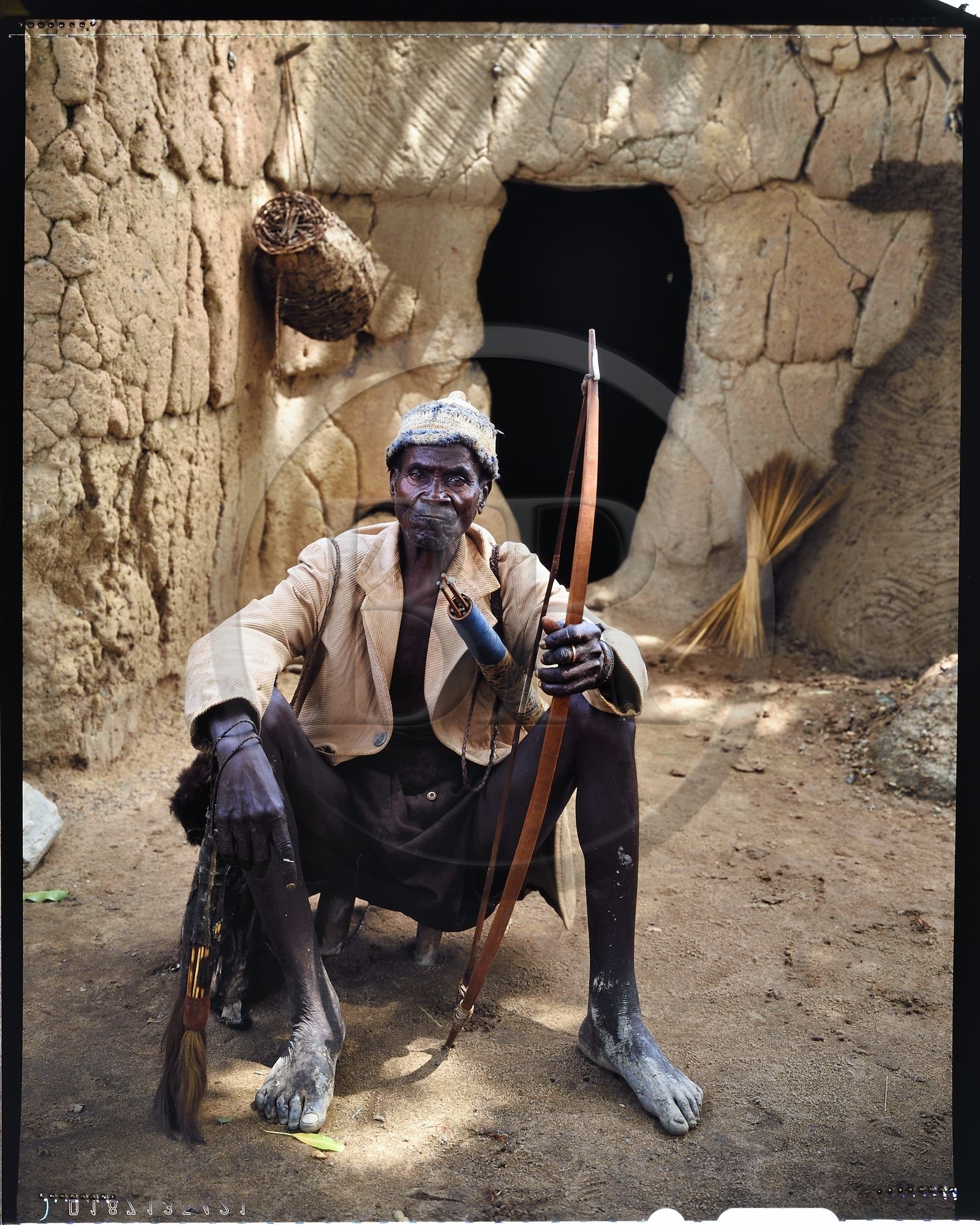 Burkina Faso, province de Poni, pays des Lobi, région de Loropéni, chef de famille dit le vieux posant avec arc et flèches devant l'entrée de sa maison au village de Lakar