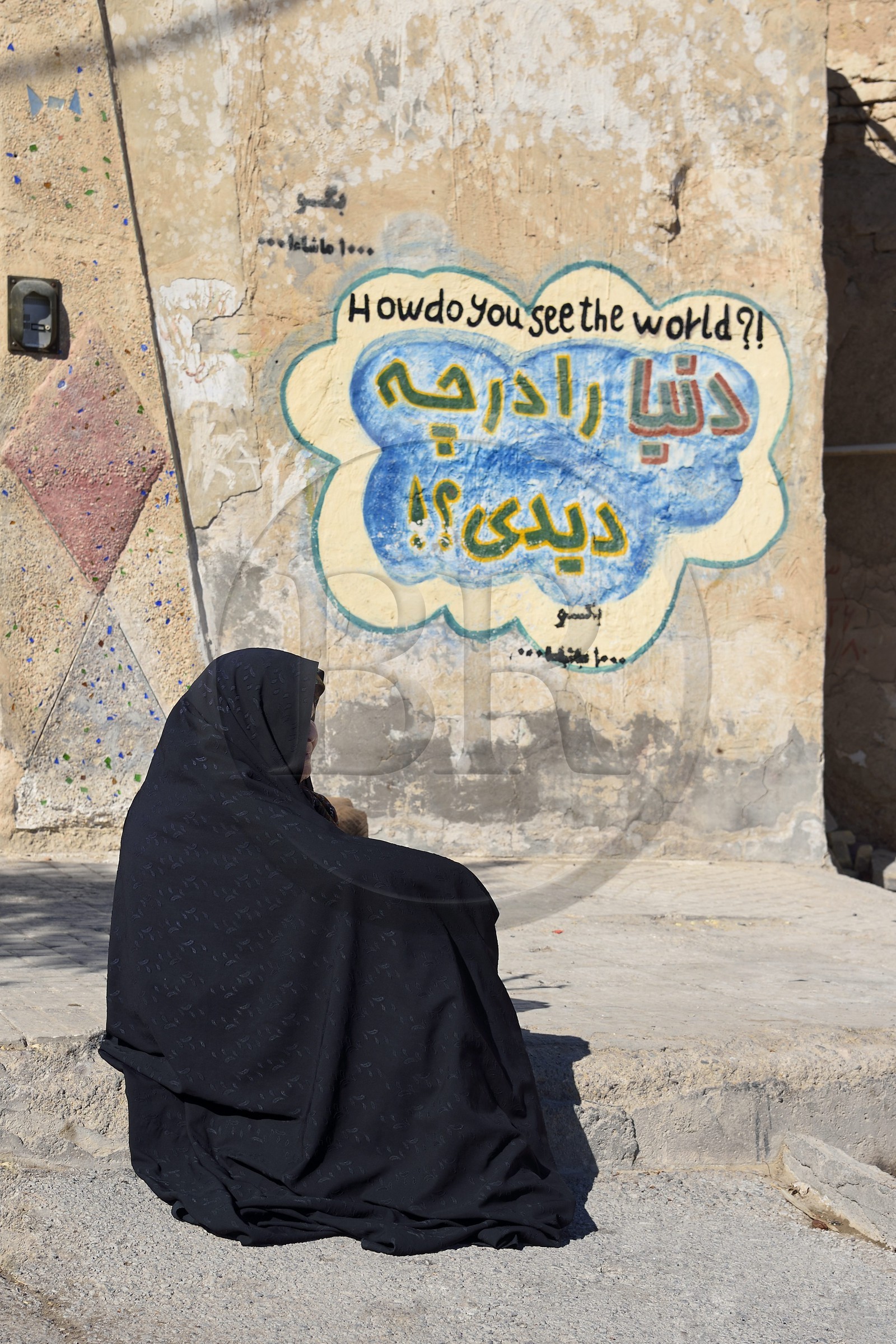 Iran, Province d'Ispahan, désert du Dasht-e Kavir, ville de Nain ou Na'in, femme devant une maison avec un graffiti affichant comment voyez vous le monde Iran, Province d'Ispahan, désert du Dasht-e Kavir, ville de Nain ou Na'in, femme devant une maison avec un graffiti affichant comment voyez vous le monde