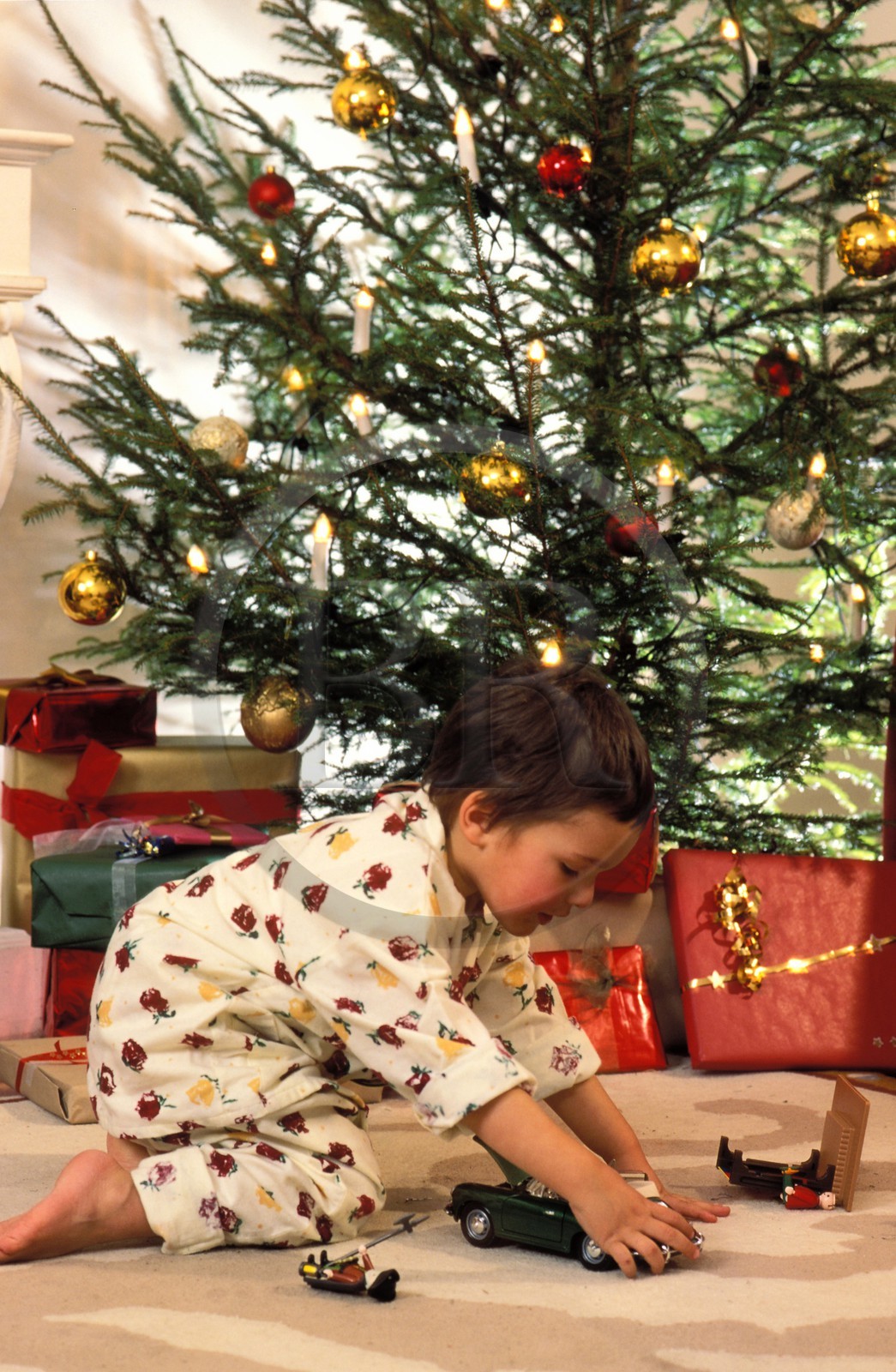 France, Noël en famille, après avoir ouvert les cadeaux, l'enfant joue devant le sapin avec une petite voiture France, Noël en famille, après avoir ouvert les cadeaux, l'enfant joue devant le sapin avec une petite voiture