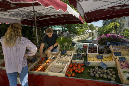 France, Vaucluse, L'Isle sur la Sorgue, market day, Justin serves a customer from his fruit and vegetable stall on a bridge over the Sorgue river