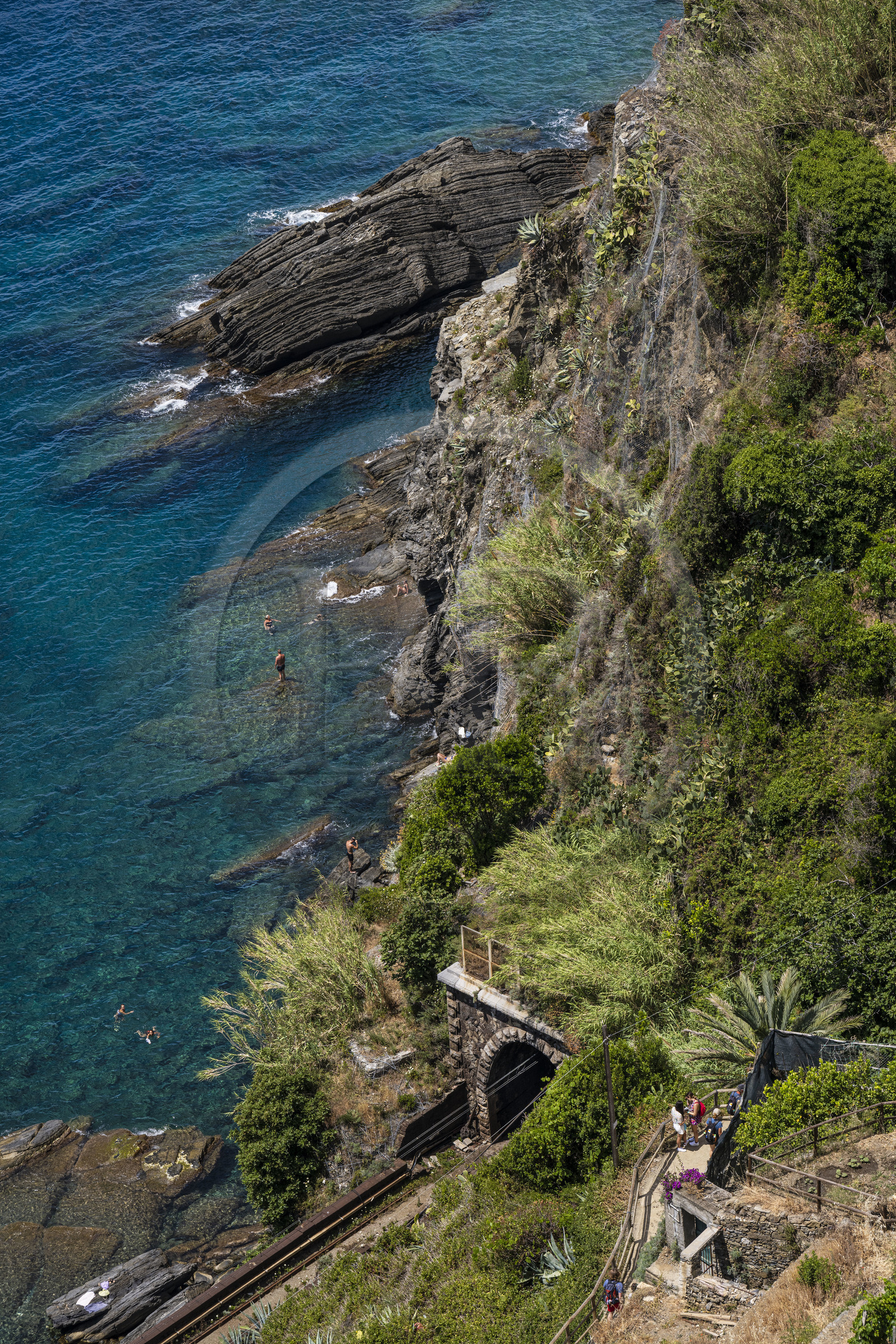 Italy, Liguria, Cinque Terre National Park listed as World Heritage by UNESCO, village of Vernazza, hikers on the GR 592 coastal path overlooking the railway line and swimmers at the foot of the cliffs Italy, Liguria, Cinque Terre National Park listed as World Heritage by UNESCO, village of Vernazza, hikers on the GR 592 coastal path overlooking the railway line and swimmers at the foot of the cliffs