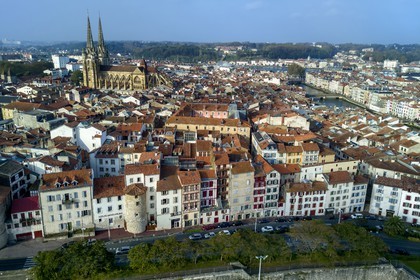 France, Pyrenees Atlantiques, Basque Country, Bayonne, the spires of St. Catherine's Cathedral behind the towers of the former ramparts integrated in the buildings of the rue Tour de Sault, the Nive river on the right and the Adour river in the background (aerial view)