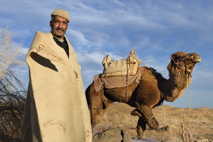 Iran, Isfahan province, Dasht-e Kavir desert, Mesr in Khur and Biabanak County, camel owner Ali Saraban wearing his grandfather camel wool felt (namad) and one of his camels at Kuh e-Sefid bivouac