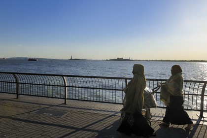 United States, New York City, Manhattan, South Point, Battery Park, veiled women walking along Battery Park and the Statue of Liberty in the background