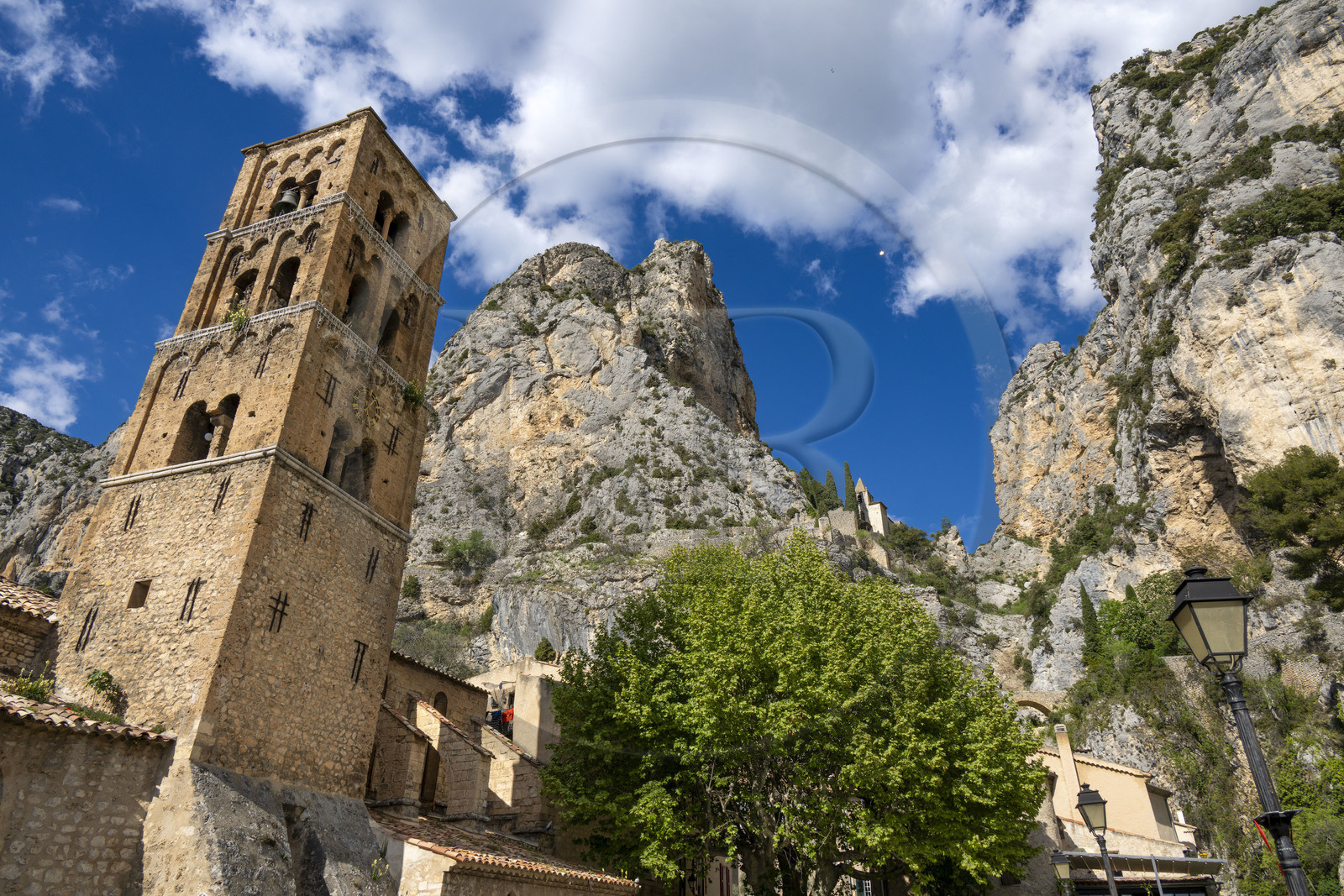 France, Alpes-de-Haute-Provence (04), Parc Naturel Régional du Verdon, Moustiers-Sainte-Marie, labellisé Les Plus Beaux Villages de France, l'église Notre-Dame-de-l'Assomption avec son clocher du XIIe siècle en tuff et la chapelle Notre-Dame de Beauvoir en arrière plan dans la falaise