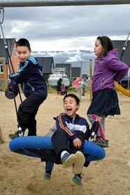Greenland, North West coast, Baffin Sea, Qaanaaq or New Thule, Inuit children play on a playground during their break, an iceberg in the background