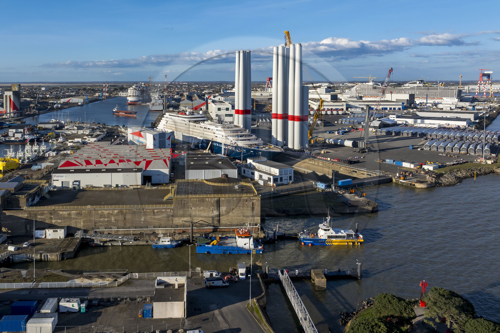 France, Loire-Atlantique (44), Saint-Nazaire, l’écluse Est et l'écluse fortifiée de l'ancienne base sous-marine allemande construite lors de la dernière guerre mondiale au premier plan et le chantier du super-yacht de luxe Ritz-Carlton Luminara dans la forme Joubert, les tours d'éoliennes à droite sont stockées avant embarquement, le paquebot de 333m MSC World America construit par les Chantiers de l'Atlantique en arrière plan (vue aérienne)