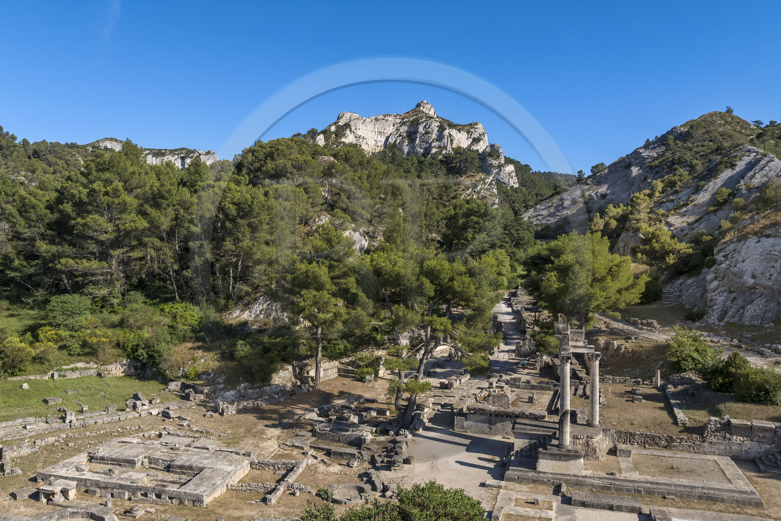 France, Bouches-du-Rhône (13), Parc Naturel Régional des Alpilles, Saint-Rémy-de-Provence, site archéologique de Glanum au pied du massif des Alpilles, colonnes et entablement reconstitués du petit temple géminé du premier forum au premier plan à droite (vue aérienne)