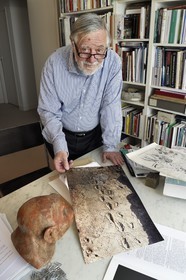 France, Paris (75), le paléontologue et paléoanthropologue Yves Coppens, professeur émérite au Collège de France, au bureau de son domicile parisien, il nous montre une photo des empreintes de pas de Laetoli sous le regard de la reproduction supposée du visage de Lucy