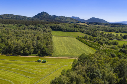 France, Puy-de-Dôme (63), Saint-Ours-les-Roches, hameau de Beauregard, tracteur récoltant le fourrage avec une presse enrubanneuse de balles de foin dans un champ, en arrière plan le volcan le Puy Chopine à gauche et le Puy de Dome à droite (vue aérienne)