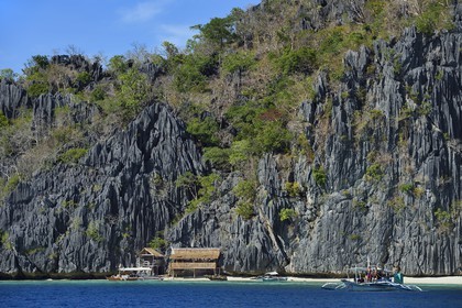 Philippines, Calamian Islands in northern Palawan, Coron Island Natural Biotic Area, Outrigger canoe and beach under giant walls of limestone cliffs
