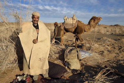 Iran, Isfahan province, Dasht-e Kavir desert, Mesr in Khur and Biabanak County, camel owner Ali Saraban wearing his grandfather camel wool felt (namad) and one of his camels at Kuh e-Sefid bivouac