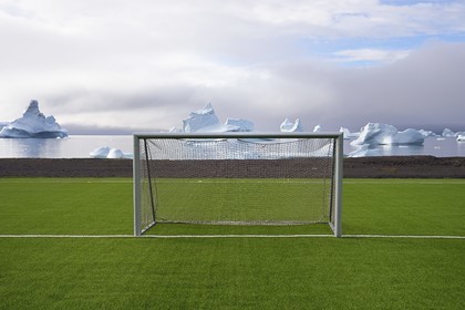 Greenland, west coast, Disko Island, Qeqertarsuaq, goal cage of a soccer field covered with synthetic grass and icebergs in the background